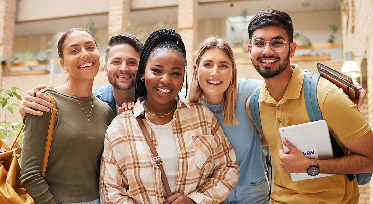 A diverse group of college students stand together outside a college building.