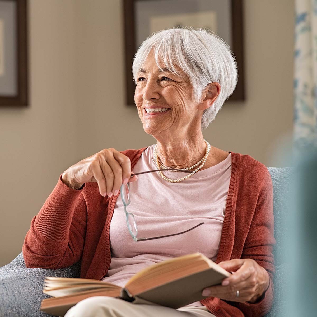 A female senior smiles while reading a book.