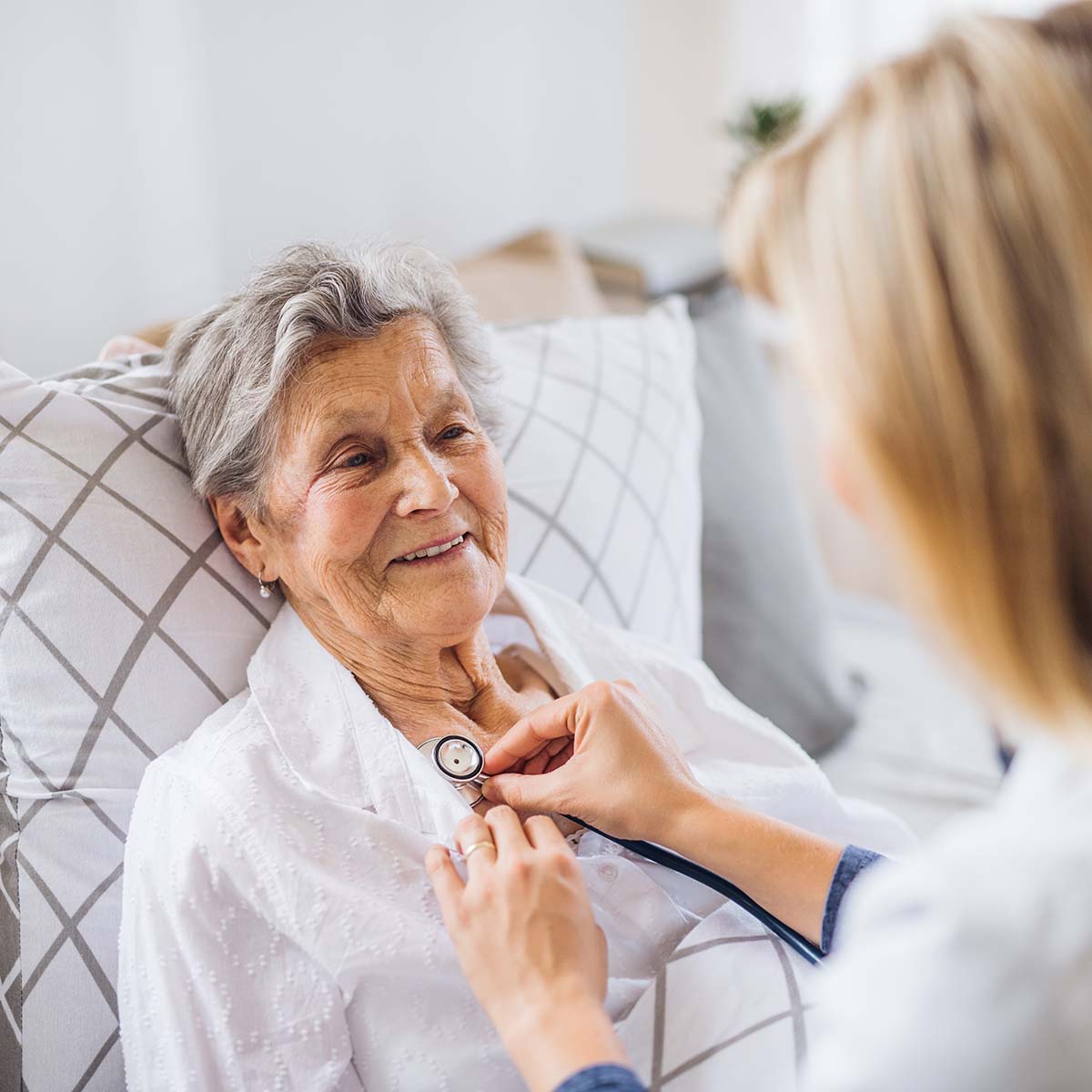 A hospice nurse provides care to a female senior at home in her bed.