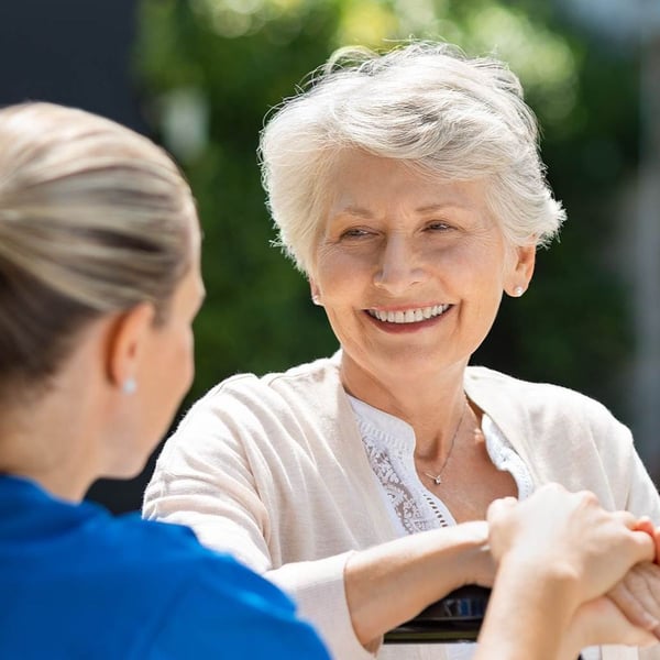 A nurse squats next to a smiling senior in a wheelchair.